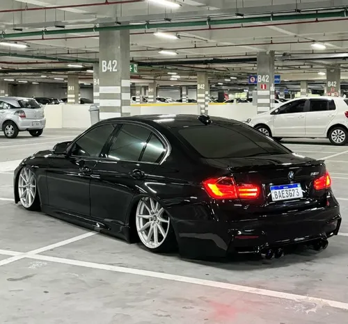  uma BMW m3 preto, com borry kit, rodas brancas largas em um estacionamento.